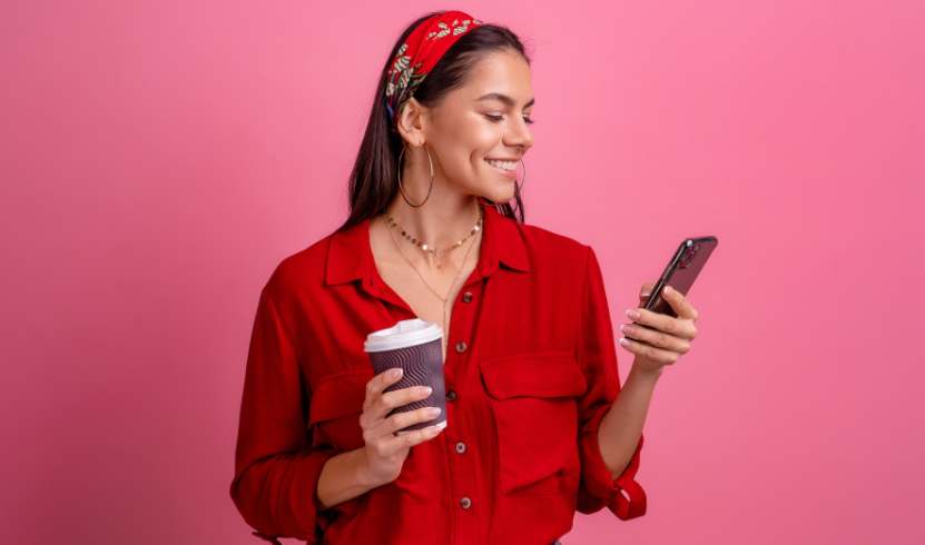 woman in red smiling at her cellphone and holding a coffee