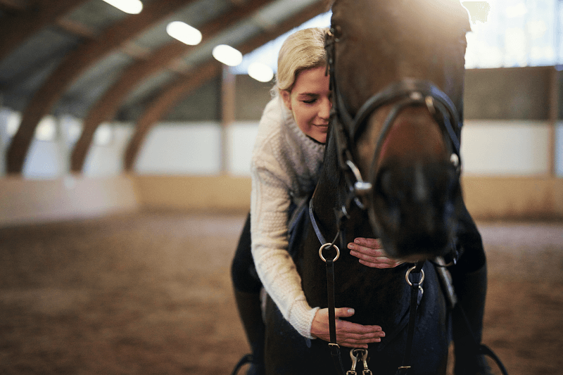 Blond woman astride horse, leaning forward hugging its neck