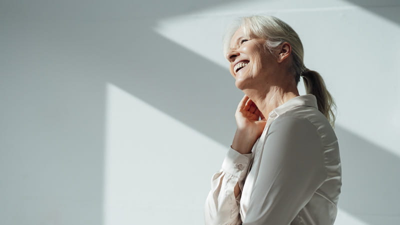 A profile view of a smiling older adult woman in strong lighting.
