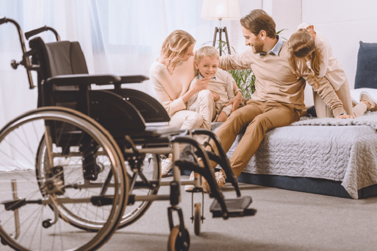 A young family is sitting on a bed next to a wheelchair.